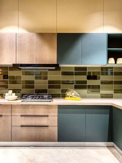 A stylish kitchen with a mix of wood and blue-grey cabinets, complemented by a glossy green subway tile backsplash.