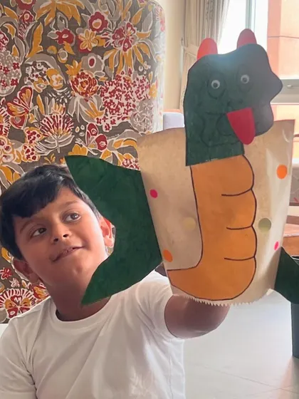 A young boy proudly holds up the dragon paper bag puppet he made. It's so rewarding to see kids excited about their own creations.