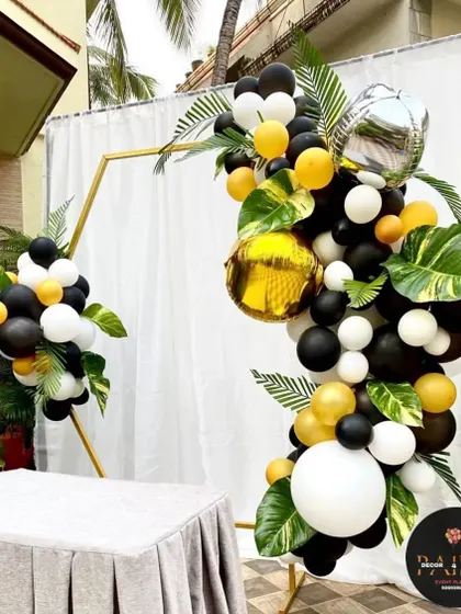 A modern hexagonal frame decorated with black, white, and yellow balloons and tropical leaves for a chic party look.