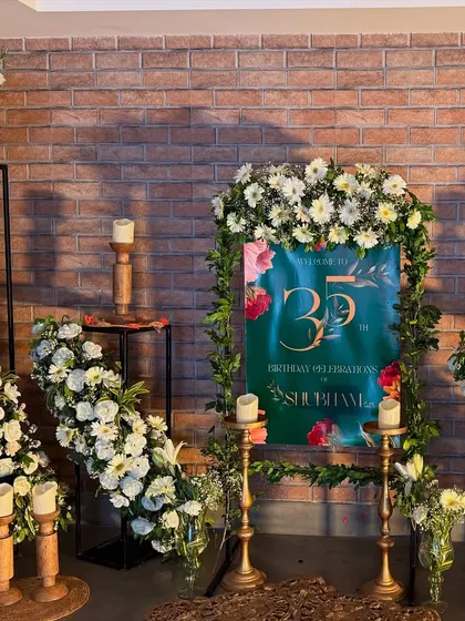 A beautiful welcome setup for a 35th birthday against a rustic brick wall. We used a custom welcome sign, cascading white floral arrangements, and candle stands to create an inviting entrance.