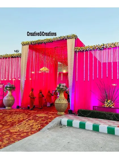 A bright and bold pink entrance for a wedding. The combination of fabric draping, hanging crystals, and floral toppers creates a festive and welcoming look.