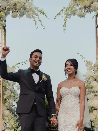 The triumphant and happy moment right after the "I do's," with the couple framed by a beautiful white floral arch.