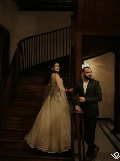 An elegant couple poses on a wooden staircase, the lighting creating a warm and classic atmosphere.