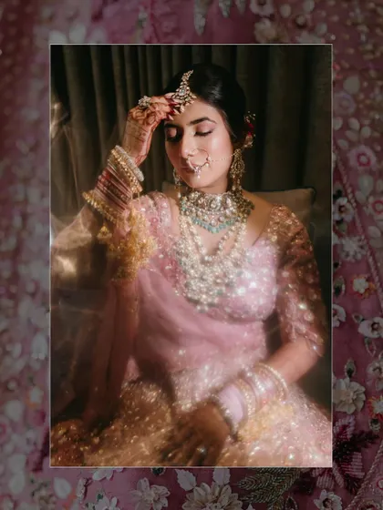 A dreamy, soft-focus portrait of a bride in her pink lehenga, adjusting her maang tikka, with a sparkling effect adding to the magic.