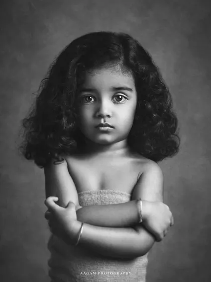 A stunning black and white portrait of a little girl with beautiful curly hair. Her direct gaze is captivating, and the monochrome style gives it a timeless, classic feel.