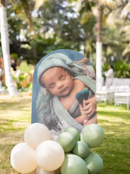 A sweet photo of a sleeping newborn displayed on a stand with green and white balloons, part of the personalized decor at Shourya's safari party.