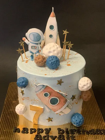 An out-of-this-world space themed cake for a 7th birthday. It's decorated with a fondant astronaut, rockets, and planets against a starry blue background.