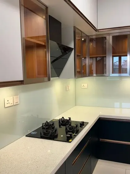 A luxury kitchen featuring two-tone cabinets with glass doors and rose gold accents. The design includes a built-in hob and a frosted glass backsplash for a sophisticated and modern look.