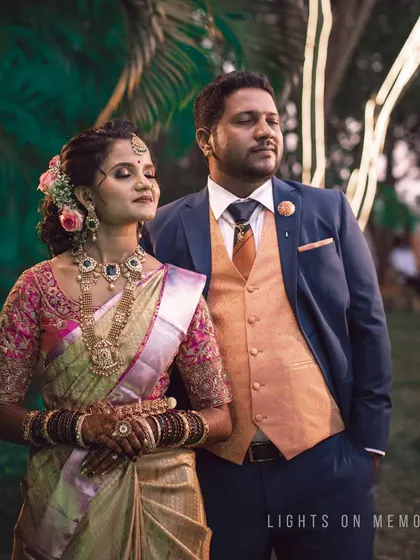 A portrait of a couple at their outdoor reception or engagement event. The bride's intricate saree and the groom's three-piece suit are perfectly captured.