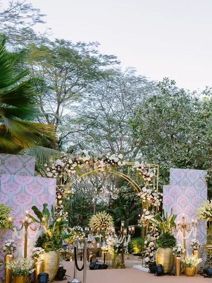 An elegant wedding entrance with golden arches, lush tropical foliage, and traditional patterned backdrops, creating a beautiful fusion of modern and heritage design.