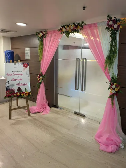 A welcoming entrance for a Roka ceremony, featuring draped curtains, floral accents, and a personalized welcome sign on an easel.
