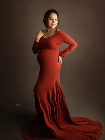 A full-length view of this elegant, long-sleeved orange gown, showing how it drapes beautifully over the baby bump.