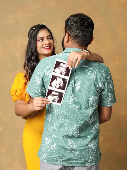 A creative and exciting pregnancy reveal. The mom-to-be hugs her partner from behind while holding up the ultrasound pictures, sharing their happy secret.