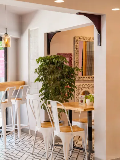 A detail shot showing the mix of materials within Qoqobae. The patterned floor tiles, white metal chairs, and indoor plants work together to create a space that feels layered, comfortable, and full of character.