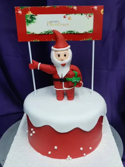 Santa Claus is coming to town! This Christmas cake features a fondant Santa topper on a bed of fluffy "snow" buttercream. It's a festive and fun addition to any holiday gathering.