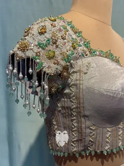 Nithya’s silver and deep green blouse with an asymmetric neckline, where one shoulder is adorned with cascading floral appliqué and beaded tassels.