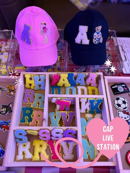 A glimpse of our live cap customization station, showing a variety of colorful chenille initial patches and character designs ready for guests to choose from. This is where the creative fun begins at your event.