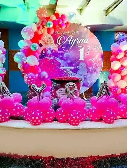 A Barbie-themed first birthday party with a vibrant pink balloon setup and character props.