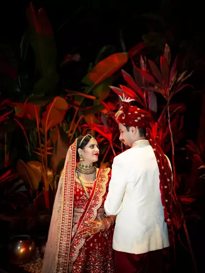 A classic wedding portrait with the couple looking at each other, set against a backdrop of lush red foliage.