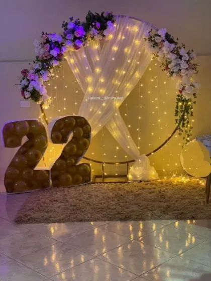 An elegant setup for a 22nd birthday, featuring a circular frame with fairy lights, drapes, and artificial flowers. The '22' is made from a balloon mosaic frame.