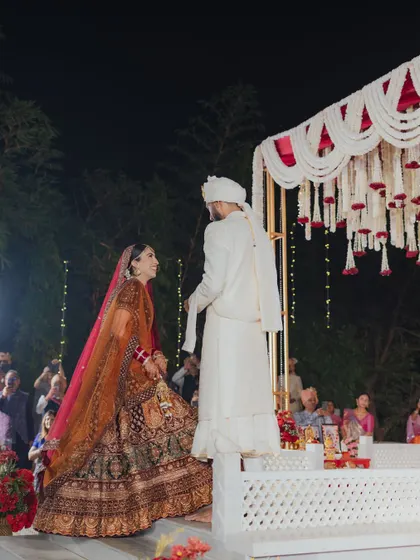 The bride and groom take their first steps towards the mandap. I designed this open-air ceremony with a clean, elevated stage and a stunning floral backdrop of white tuberoses and red roses to create a classic and dramatic effect.