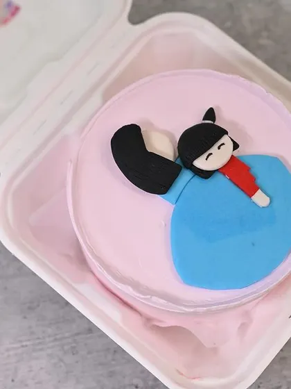 This bento cake for Daughter's Day features a cute fondant figurine of a girl, making it a personalized and adorable treat.