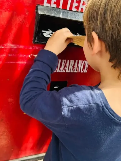 A close-up of a child posting his letter, connecting classroom learning about community helpers to a practical activity.