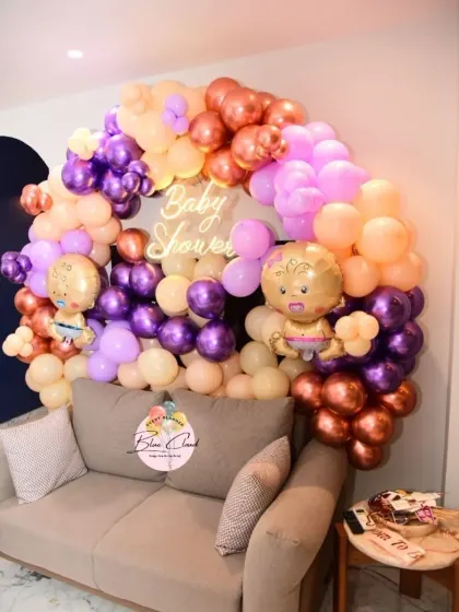 A chic baby shower setup with an organic balloon garland in purple, peach, and chrome tones, complete with a neon sign.