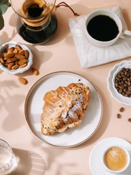 A wider, flatlay view of the almond croissant and coffee setup. This type of shot is great for website banners or magazine features, showing the product in a full, styled scene.