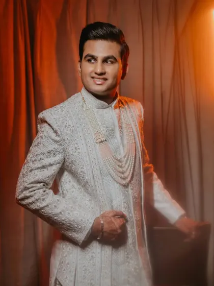 A handsome portrait of the groom in his white sherwani, illuminated by warm, dramatic lighting. This shot captures his confident and happy demeanor before the ceremony.