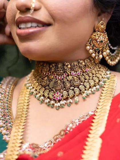 A close-up of a bride's smile, highlighting her stunning traditional gold choker necklace with intricate temple designs.