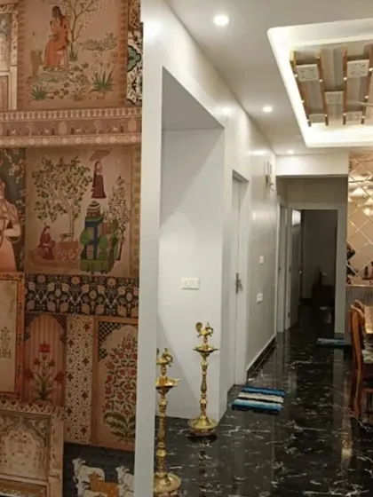 A collage-style wallpaper featuring various scenes from Indian miniature paintings, creating a rich, textured, and culturally significant feature in a hallway.