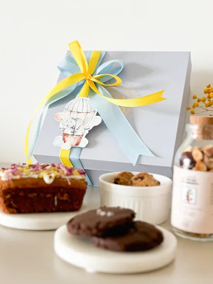 Celebrate the miracle of life with a thoughtful gift. This baby announcement hamper features a personalized box, a mini loaf cake, our signature cookies, and a bottle of healthy granola.