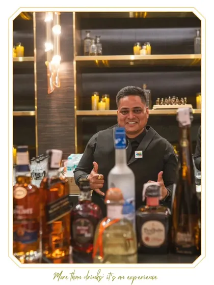 A smiling bartender giving a thumbs-up behind a fully stocked premium bar. His positive attitude is representative of our entire team's approach to hospitality.