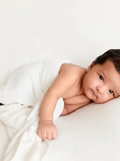 An awake newborn lies on a clean white surface, wrapped loosely to allow for natural movement and capture their curious expression.