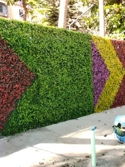 This outdoor artificial green wall features a colorful chevron pattern, creating a vibrant and eye-catching display.