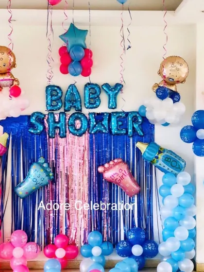 A classic baby shower home decoration. The setup includes a blue foil curtain backdrop and a balloon arrangement in pink and blue for a gender reveal.