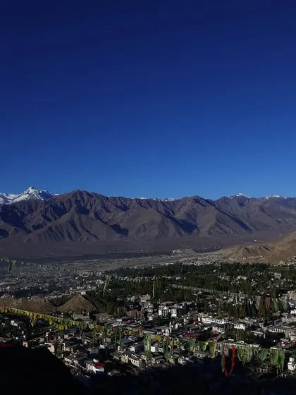 A stunning panoramic shot of Leh city from above, showcasing the sprawling town surrounded by the vast mountain landscape.