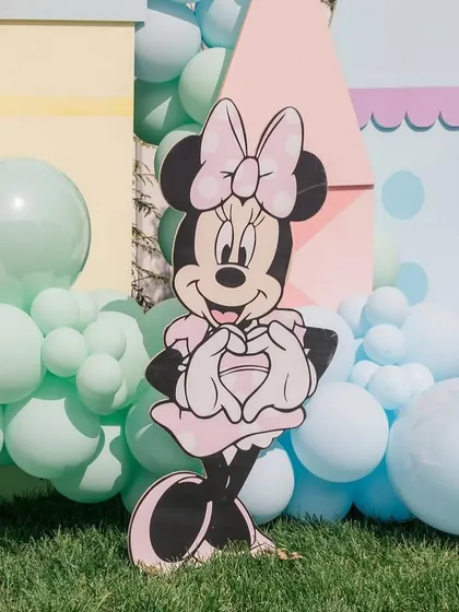 A cute Minnie Mouse cutout peeking out from behind a castle prop and a sea of pastel balloons.
