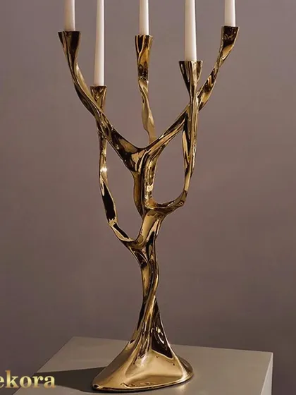 An artistic, tree-like candelabra crafted from polished gold metal. This sculptural piece holds five candles and serves as a dramatic centerpiece for a dining table or boardroom.