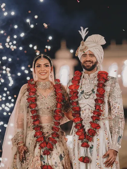 A beautiful portrait of the couple, smiling and radiant, with their intricate rose varmalas and a backdrop of sparkling lights.