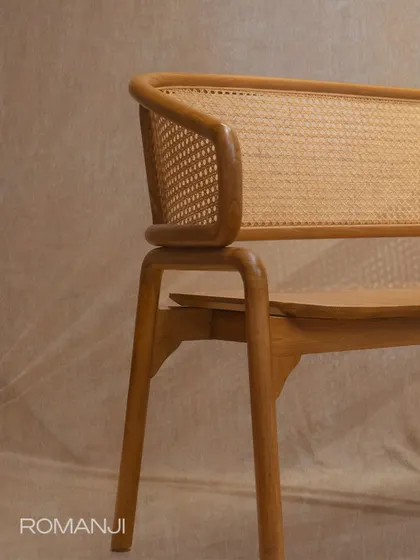 A side view of the 'Romanji' bench, highlighting the clean lines of its teak frame and the gentle curve of the armrest.