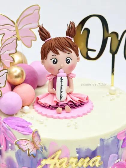 A beautiful first birthday cake with a butterfly theme. The centerpiece is a sweet baby girl figurine, surrounded by pastel buttercream strokes and delicate butterflies.