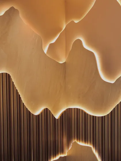 A close-up of the custom-designed, back-lit wall feature. The soft glow emphasizes the organic, layered forms and the texture of the fluted paneling below, creating a piece that is both architecture and art.