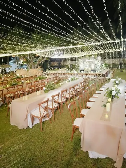 An enchanting welcome dinner setup under a canopy of fairy lights, with long tables arranged for a communal and celebratory meal.