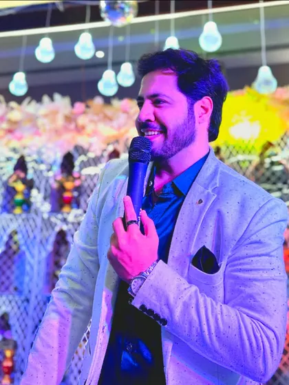 A close-up shot of me hosting, with the beautiful, softly lit decor of a Sangeet night in the background.