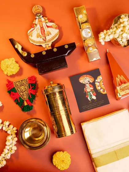 A deconstructed view of the 'Kasavu & Katha' hamper, highlighting each traditional element like the kasavu cloth, brassware, and handcrafted decor against a vibrant orange background.