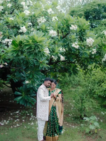 A full-length portrait of the couple standing under a flowering tree, a classic and romantic setting for an engagement photo.