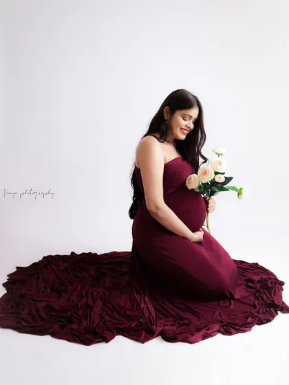 A duplicate of image 150, this sweet portrait shows a mom-to-be kneeling in a rich burgundy gown, holding a small bouquet of white roses.