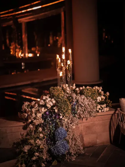 An outdoor seating area was made intimate with a cascading floral arrangement along a stone ledge. The warm candlelight reflects beautifully, creating a cozy and elegant space for guests to converse during the party.
